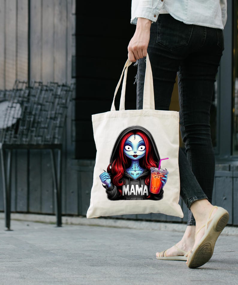 May include: Cream-colored tote bag featuring a cartoon character with blue skin, red hair, and a black hoodie with the word "MAMA". The character is holding a drink with a pink straw. The bag has long handles.