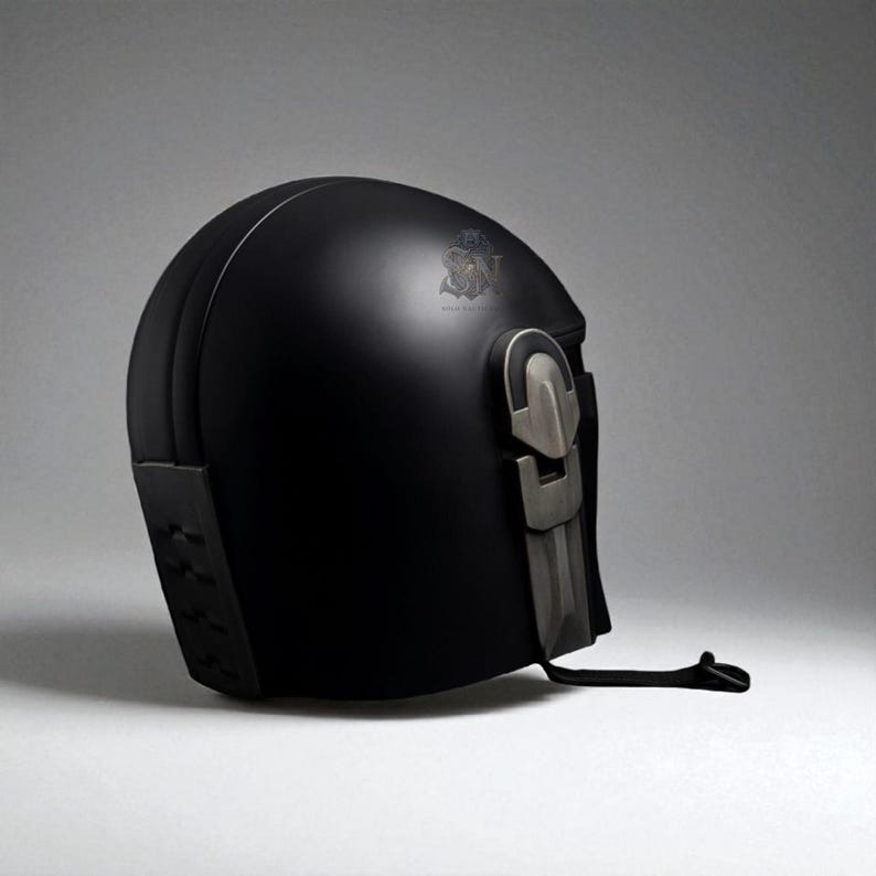 May include: A matte black helmet with a silver-colored visor and accents. The helmet has a rounded top and a detailed, angular design on the lower back. A black strap hangs from the side. The helmet is likely for cosplay or costume use.