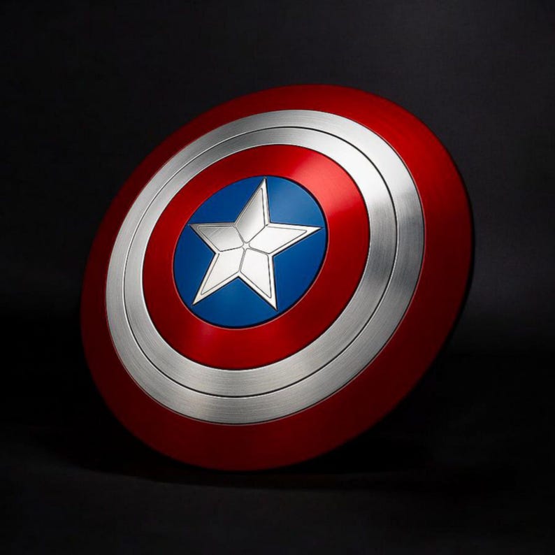 May include: A circular shield in red, white, and blue, featuring a silver star at its centre. The shield has a red outer ring, a silver middle ring, and a blue central area. This is a replica of Captain America's shield.