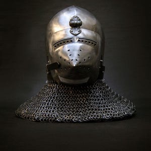 May include: A polished metal helmet with a pointed visor and numerous small ventilation holes. The helmet features a decorative crest and is connected to a chainmail coif. The medieval-style helmet is set against a dark background.