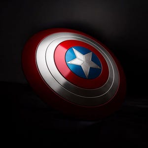 May include: A red, white, and blue shield with a silver star in the center. The shield has a circular design with concentric rings of red, silver, and blue. The shield is a prop or collectible.