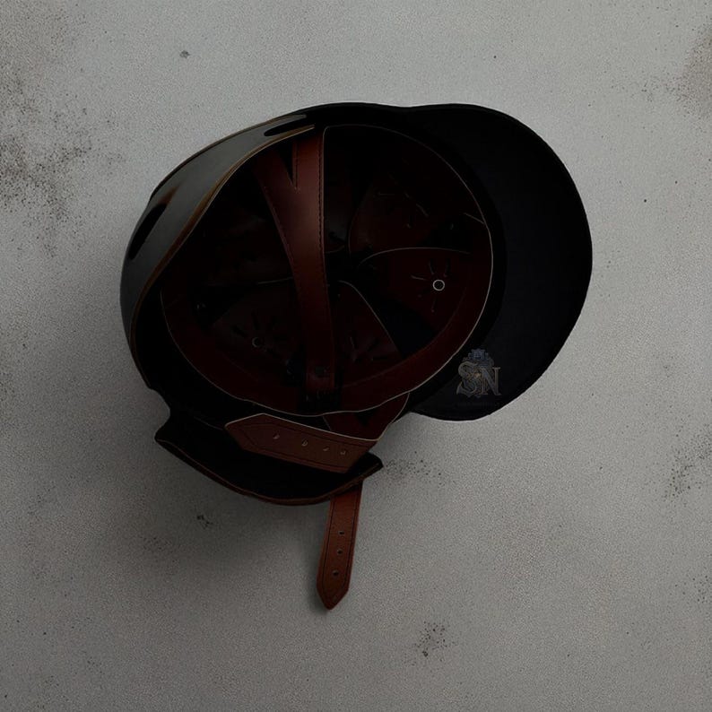 以下が含まれることがあります： 茶色の革の内装とあご紐が付いた黒いヘルメット。ヘルメットはバイザー付きの丸みを帯びた形状で、耐久性のある素材で作られている可能性があります。内部には、しっかりとフィットするように革製のストラップが付いています。