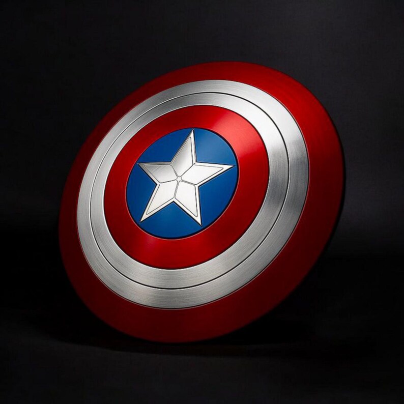 May include: A circular shield in red, white, and blue, featuring a silver star at its centre. The design includes a red outer ring, a silver band, and a blue central area. This shield is a replica of Captain America's iconic shield.