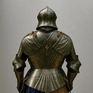 May include: A detailed view of antique metal armor, showcasing a helmet and the back of the suit. The armor has intricate designs and a fleur-de-lis emblem. The lower portion of the armor is partially visible, with blue and tan fabric.
