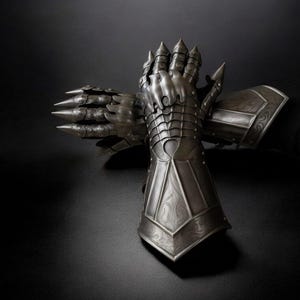 May include: A pair of intricately detailed, silver-colored gauntlets, likely for armor. The gauntlets feature articulated plates, sharp spikes, and decorative patterns. The background is a dark, solid color, emphasizing the metallic texture and craftsmanship of the gloves.
