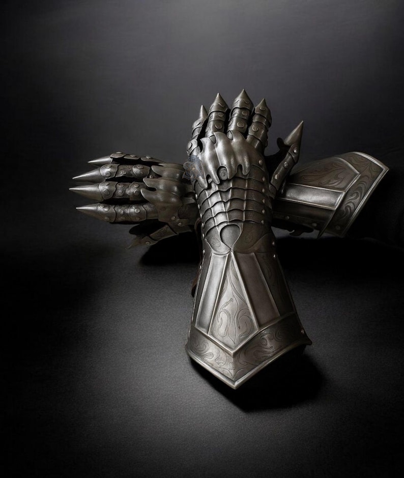 May include: A pair of intricately detailed, silver-colored gauntlets, likely for armor. The gauntlets feature articulated plates, sharp spikes, and decorative patterns. The background is a dark, solid color, emphasizing the metallic texture and craftsmanship of the gloves.