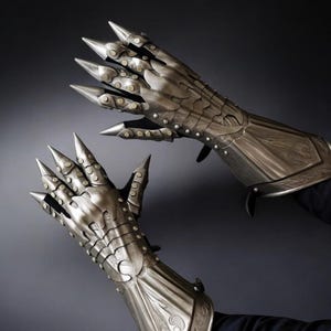May include: A pair of silver-colored metal gauntlets with long, pointed claws. The gauntlets have intricate detailing, including rivets and decorative patterns. The design suggests a fantasy or medieval theme.