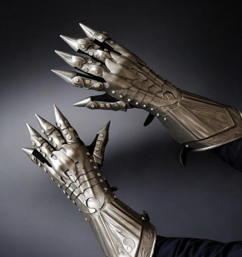 May include: A pair of silver-colored metal gauntlets with long, pointed claws. The gauntlets have intricate detailing, including rivets and decorative patterns. The design suggests a fantasy or medieval theme.