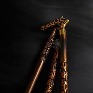 Pode incluir: Bengala de madeira castanha escura com entalhes florais intrincados e detalhes dourados. A bengala dobrável tem uma pega e um eixo decorativos. A bengala é um acessório elegante, com um mecanismo de dobragem para fácil arrumação.