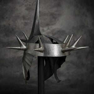 May include: A silver-colored helmet with multiple sharp spikes. The helmet has a tall central spike and several smaller spikes around the crown. The design is detailed and appears to be made of metal, with a dark background.