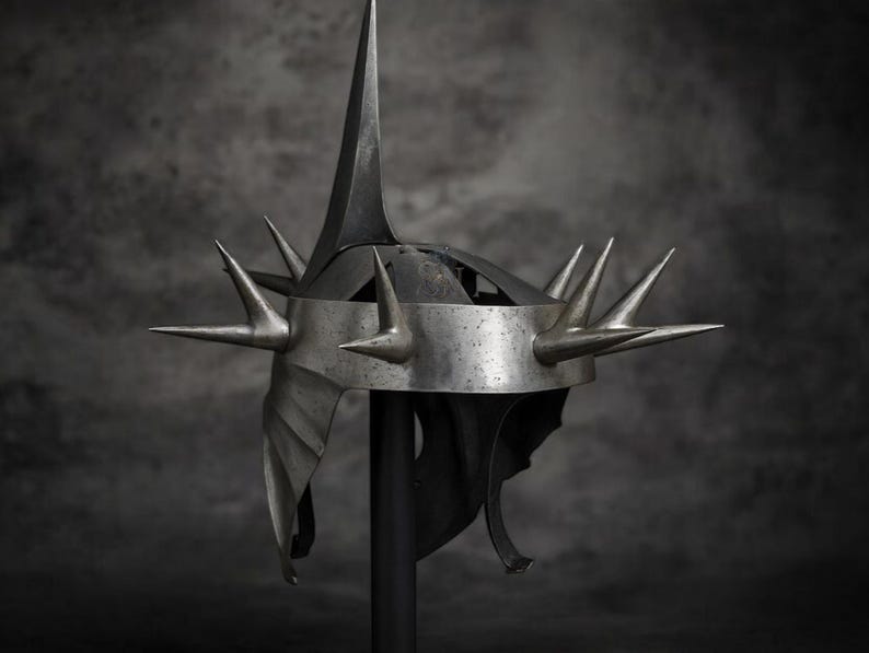 May include: A silver-colored helmet with multiple sharp spikes. The helmet has a tall central spike and several smaller spikes around the crown. The design is detailed and appears to be made of metal, with a dark background.