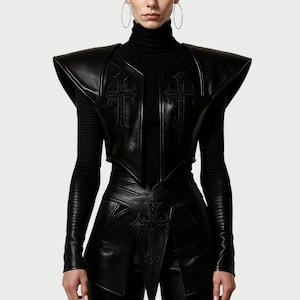 May include: Black leather vest with cross details. The vest features a structured design with shoulder pads and a fitted waist. The front of the vest and waist area are adorned with embossed cross motifs. The vest is worn over a black long-sleeved top.