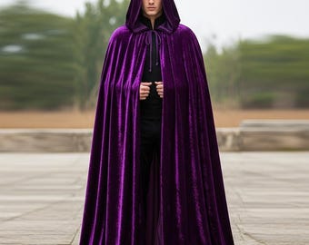 May include: A long, hooded cloak in a rich, deep purple velvet. The cloak drapes to the ground and is tied at the neck with a matching cord. The person is wearing a black shirt and pants.