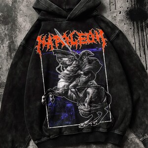 Może przedstawiać: Czarna bluza z kapturem z grafiką jeźdźca na koniu, napisem "NAPOLEON" w kolorze pomarańczowym i postarzanym wykończeniem. Projekt przedstawia postać przypominającą czaszkę i miecz. Bluza ma kaptur ze sznurkiem i kieszeń typu kangur.