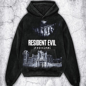 Könnte beinhalten: Schwarzer Kapuzenpullover mit dem Text "RESIDENT EVIL. requiem" in Weiß. Das Design zeigt ein Monstergebiss und ein Graustufenbild eines Gebäudes. Der Hoodie hat eine Kängurutasche und eine Kapuze.