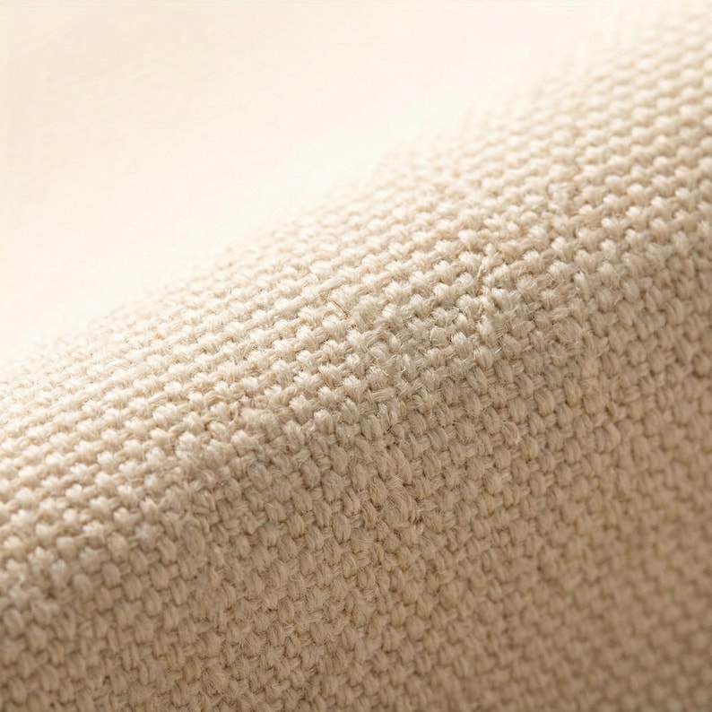 Puede incluir: Primer plano de una tela beige tejida con una superficie texturizada. La tela parece estar tejida apretadamente, con un patr&oacute;n visible de hilos que se cruzan. El color es un tono c&aacute;lido y neutro.