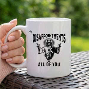 May include: A white ceramic mug with a black handle and the text "But First, Coffee" in a bold, black font. The mug is set against a blurred background, suggesting a cozy setting.