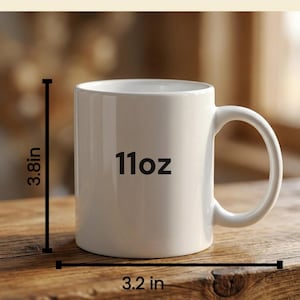 Puede incluir: Una taza de cer&aacute;mica blanca con un asa curvada. La taza est&aacute; etiquetada como "11oz" y mide 9,6 cm de alto y 8,1 cm de ancho. La taza est&aacute; sobre una superficie de madera.