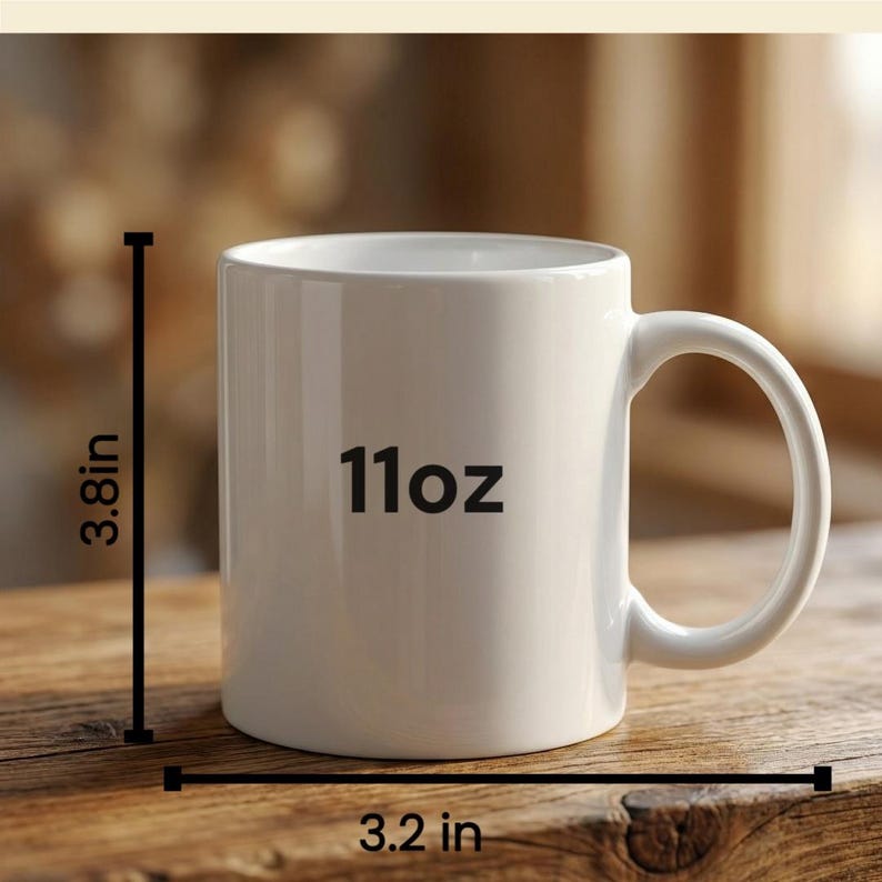 Puede incluir: Una taza de cer&aacute;mica blanca con un asa curvada. La taza est&aacute; etiquetada como "11oz" y mide 9,6 cm de alto y 8,1 cm de ancho. La taza est&aacute; sobre una superficie de madera.
