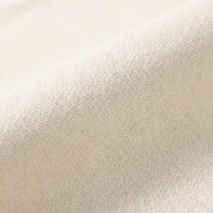 Puede incluir: Primer plano de una tela de lona blanquecina texturizada. El tejido del material es visible, creando un patr&oacute;n sutil. La tela est&aacute; ligeramente curvada, mostrando la textura y la profundidad del material. El color es un tono c&aacute;lido y neutro.