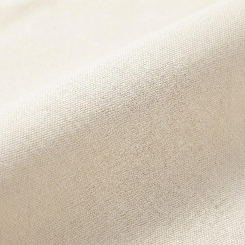 Puede incluir: Primer plano de una tela de lona blanquecina texturizada. El tejido del material es visible, creando un patr&oacute;n sutil. La tela est&aacute; ligeramente curvada, mostrando la textura y la profundidad del material. El color es un tono c&aacute;lido y neutro.