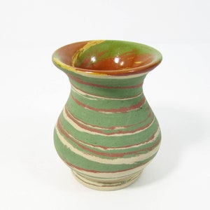 May include: A small, green, white, and orange ceramic vase with a marbled design. The vase has a wide mouth and a rounded body.