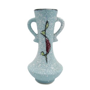 May include: A light blue ceramic vase with two handles and a speckled texture. The vase features a vertical design with red, green, and black accents. The vase is approximately 7 inches tall.