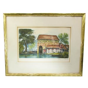 May include: A framed watercolor painting of a building with a red roof and a watermill. The building is surrounded by trees and a river. The painting is signed "Flavien. Roll"