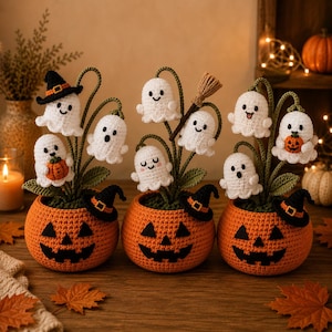 May include: Three crocheted orange pumpkin pots, each featuring a black jack-o'-lantern face. Each pot contains green stems with multiple small white crocheted ghosts, some wearing black witch hats, holding tiny pumpkins, or carrying a broom.