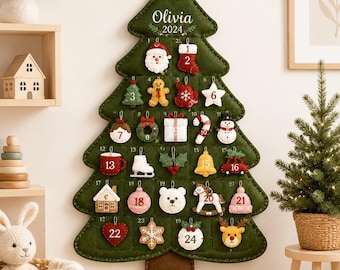 以下が含まれることがあります： 上部にOliviaと2024の刺繍が施された、クリスマスツリー型の濃い緑色のフェルト製壁掛けアドベントカレンダー。24個の番号付きポケットがあり、それぞれに小さくカラフルなフェルト製のクリスマスオーナメントが入っています。