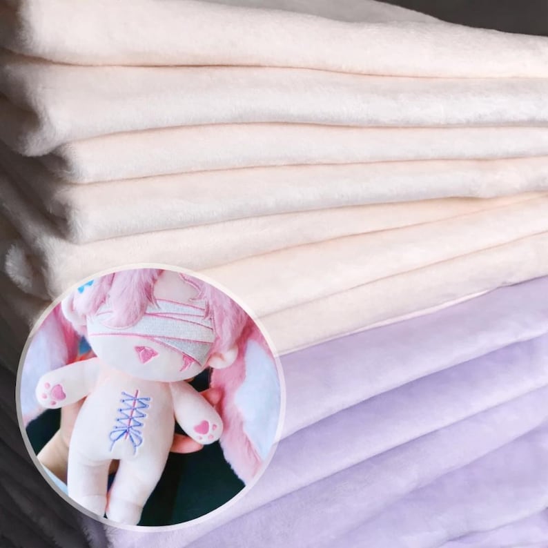 K&ouml;nnte beinhalten: Ein Stapel weicher, hellfarbener Stoffe mit einer Pl&uuml;schstruktur. Ein kreisf&ouml;rmiger Einsatz zeigt ein Pl&uuml;schkaninchen mit rosa Akzenten, einschlie&szlig;lich Ohren, Bandagen und herzf&ouml;rmigen Pfoten. Das Kaninchen hat ein blaues Korsettmuster auf der Brust.