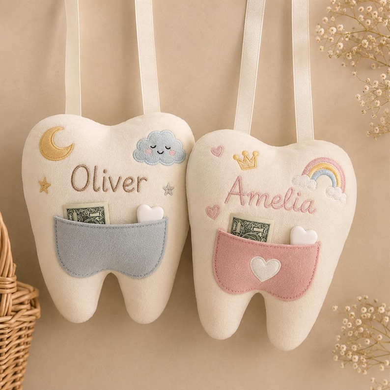 May include: Two cream-coloured felt tooth-shaped pillows with hanging straps. One features the name Oliver, a yellow moon, and a blue cloud above a blue pocket. The other features the name Amelia, a yellow crown, and a rainbow above a pink pocket.