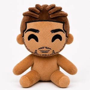 May include: A plush doll with a brown complexion, brown hair, and a stylized face. The doll has black embroidered eyebrows, eyes, and a goatee. The doll is sitting with its arms outstretched and has a light brown body.