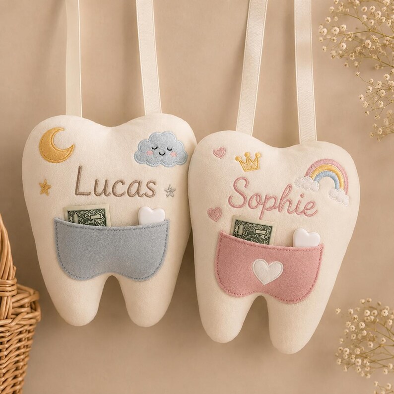 May include: Two cream-coloured tooth-shaped plush pillows with hanging ribbons. The left pillow features a blue pocket, a yellow moon, and the name Lucas. The right pillow features a pink pocket, a gold crown, a rainbow, and the name Sophie.
