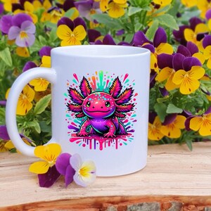 Pu&ograve; includere: Tazza in ceramica bianca con un'illustrazione colorata di un axolotl. L'axolotl &egrave; raffigurato in tonalit&agrave; di rosa, viola e blu, con vivaci spruzzi di colore intorno. La tazza ha un manico curvo ed &egrave; circondata da fiori gialli e viola.