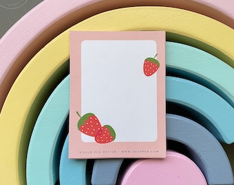 May include: A pink, yellow, blue, and gray rainbow wooden toy with a white card on top. The card has a pink border and a white interior with a strawberry graphic and the text "Sour Pea Design - www.sourpea.com".