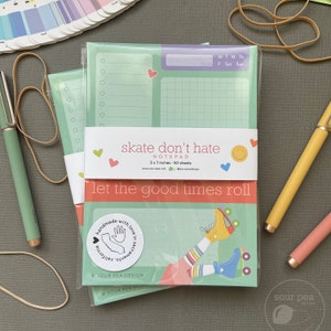 May include: A set of two green and white notepad packs with a roller skate design. The notepad packs are wrapped in clear plastic and feature the text "skate don't hate" and "let the good times roll". The notepads are 5x7 inches and have 50 sheets each.