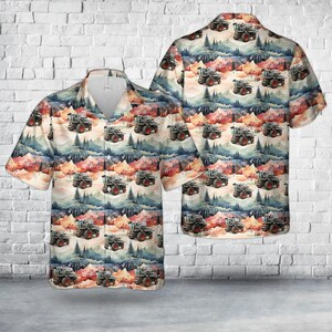Puede incluir: Camisa de manga corta con diseño de acuarela de tractores en un paisaje montañoso. La camisa tiene un cuello beige claro y un estampado de tractores, árboles y montañas en tonos grises, rojos, azules y naranjas.