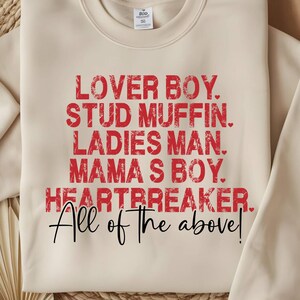 以下が含まれることがあります： クリーム色のスウェットシャツ。赤字で「LOVER BOY. STUD MUFFIN. LADIES MAN. MAMA'S BOY. HEARTBREAKER.」と書かれています。下には黒い筆記体で「All of the above!」と書かれています。カジュアルで着心地の良い衣服です。