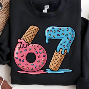 May include: Black sweatshirt with a colorful graphic of the number 67. The numbers are designed to look like ice cream cones and donuts with sprinkles. The number 6 is a pink donut with sprinkles, and the 7 is blue with sprinkles.