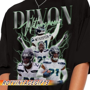 May include: Black t-shirt featuring a graphic of football player Devon Witherspoon with the text "DEVON Witherspoon" in a green and silver design. The shirt also includes the text "ROYVINTAGEGIFTS".