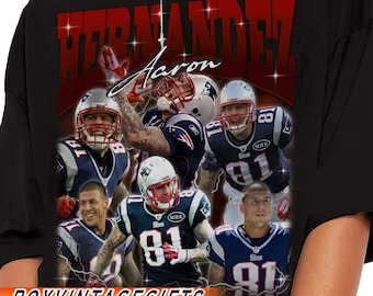 May include: Black t-shirt featuring a collage of football players in blue and white uniforms. The name "HERNANDEZ" is displayed in red, with "Aaron" in white script. The text "ROYVINTAGEGIFTS" is at the bottom.
