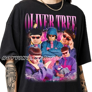 May include: A black t-shirt featuring a graphic print of Oliver Tree in various poses wearing a blue and pink jacket and red sunglasses. The text OLIVER TREE appears in large pink and purple gradient letters at the top, with ROYVINTAGEGIFTS printed across the center. The design includes lightning and cloud elements.