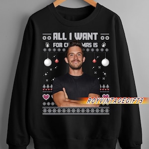 May include: Black sweatshirt with the text "ALL I WANT FOR CHRISTMAS IS" above a photo of a man. The design includes white and red Christmas ornaments and snowflake patterns. The brand name "ROYVINTAGEGIFTS" is printed on the bottom.