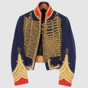 May include: A navy blue military-style jacket with gold rope detailing and gold embroidery. The jacket features a red collar and red accents on the sleeves. The jacket is hanging on a wooden hanger.