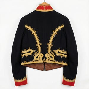 May include: A black jacket with gold embroidery and red accents. The jacket features ornate gold detailing along the seams and around the collar and cuffs. The jacket is hanging on a wooden hanger.