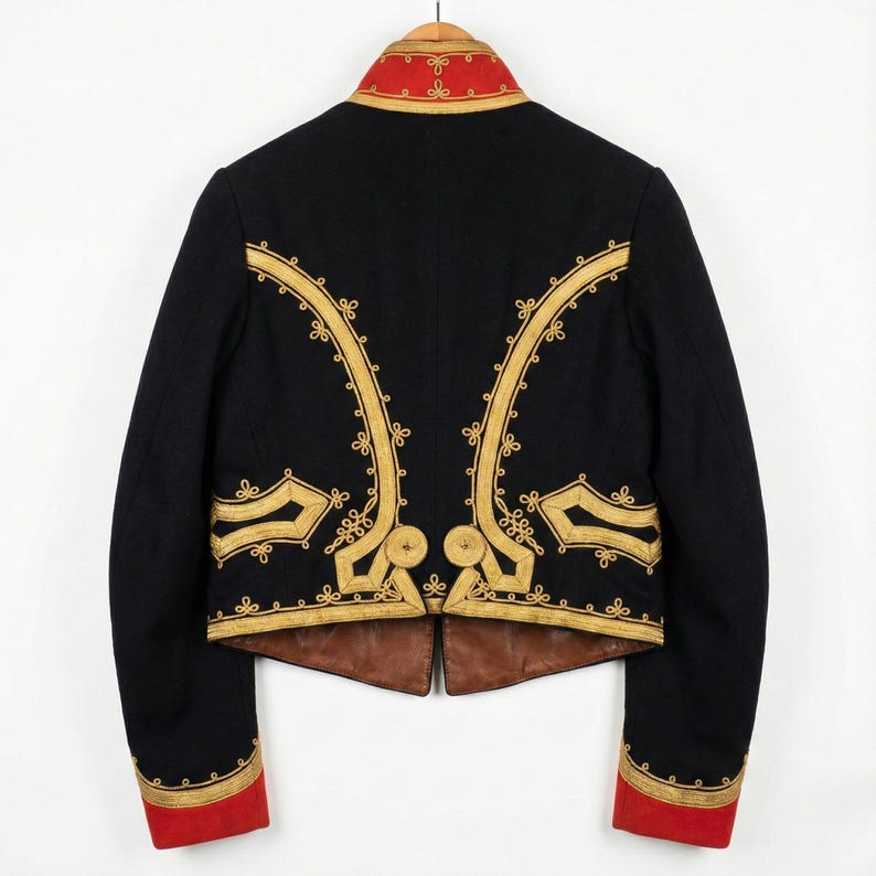 May include: A black jacket with gold embroidery and red accents. The jacket features ornate gold detailing along the seams and around the collar and cuffs. The jacket is hanging on a wooden hanger.