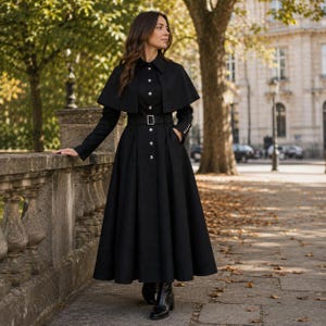 Könnte beinhalten: Ein langärmeliges schwarzes Mantelkleid mit strukturiertem Kragen, durchgehender Knopfleiste und passendem Gürtel mit rechteckiger Schnalle. Das Kleidungsstück verfügt über einen capeartigen Überwurf an den Schultern und einen langen Faltenrock.