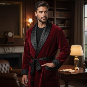 May include: A burgundy velvet robe with black quilted lapels, cuffs, and belt. The robe has a tie closure and pockets. The image is set in a room with a fireplace, bookshelves, and a table lamp.