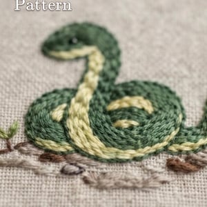 Op de afbeelding: Een borduurpatroon van een opgerolde slang in donkergroene en lichtgele tinten op een beige stoffen achtergrond. De tekst "PDF Pattern" staat linksboven en de tekst "lumellu.etsy.com" staat onderaan in het midden van de afbeelding.